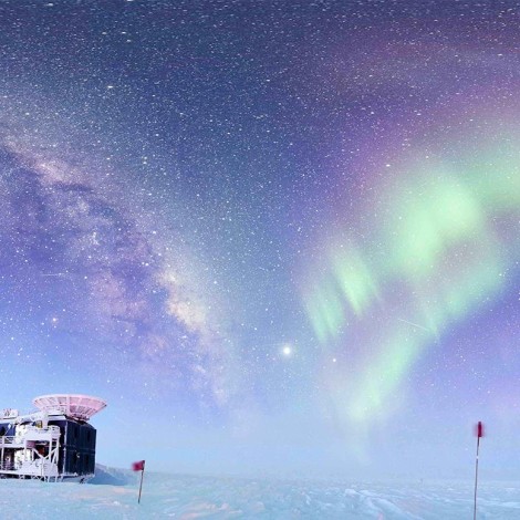 A radio telescope located on an icy plain in Antarctica, with an aurora in the sky overhead.