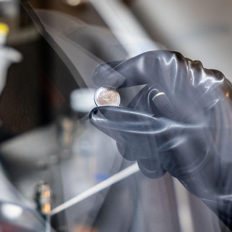 A closeup of a gloved hand holding a battery in the shape of a flat disc